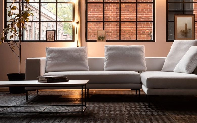 Canapé d'angle Clémenceau en tissu blanc, installé dans un espace au style sobre et industriel.
